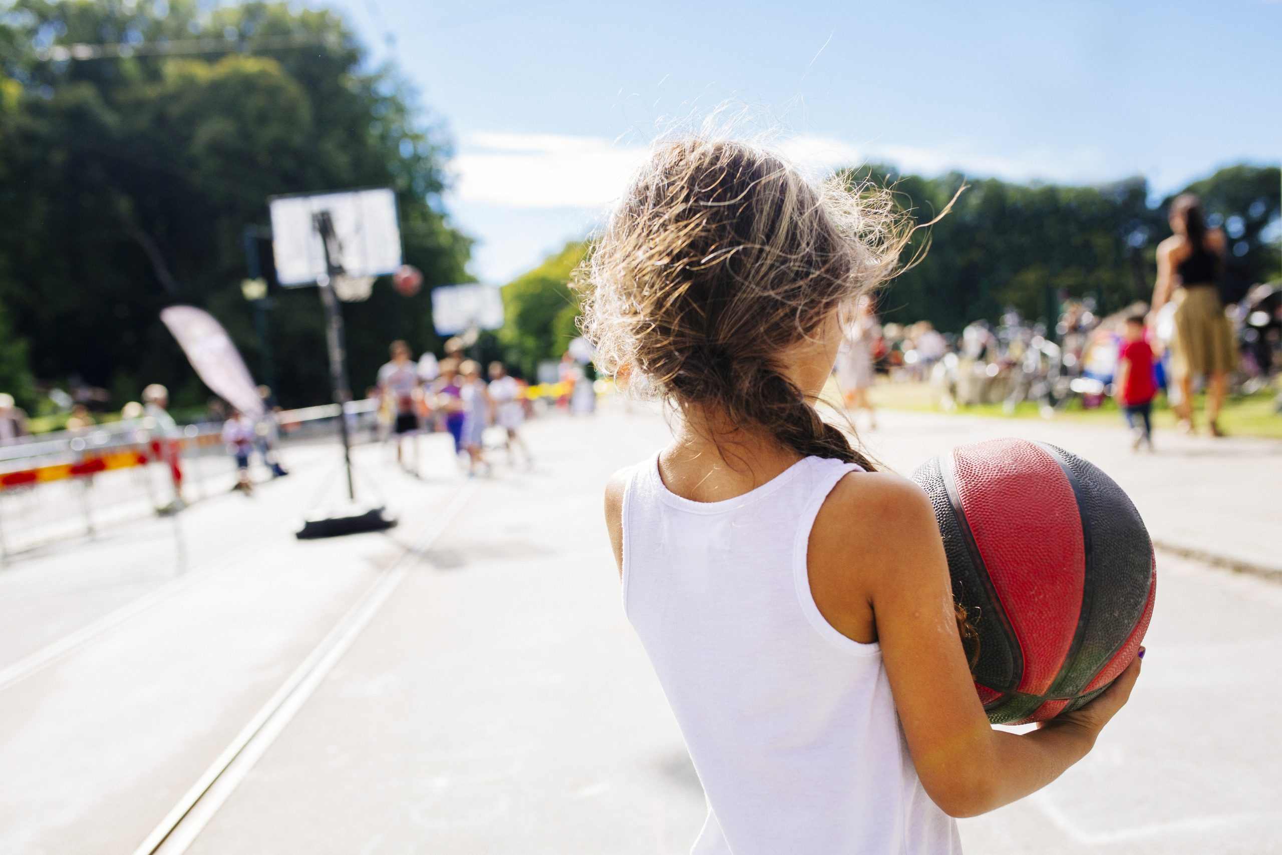 Petite fille vue de dos qui tient un ballon de basketball sur un terrain extérieur